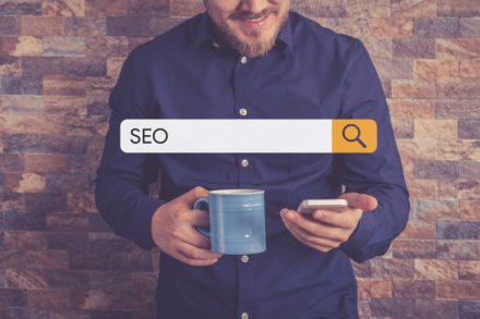 Person in blue shirt holding a phone and a mug. Search bar with "SEO" over the top.